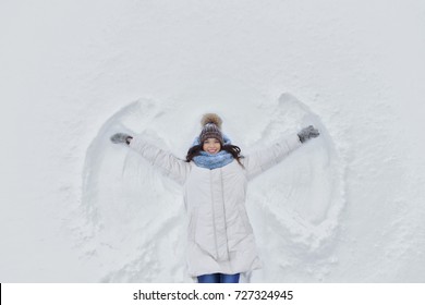 Young Smiling Woman Kidding On Snow In Winter Day. The Girl On A Snow Angel Shows. Copyspace