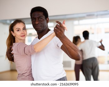 Young Smiling Woman Learning To Dance Waltz Paired With African American Man In Dancing Class..