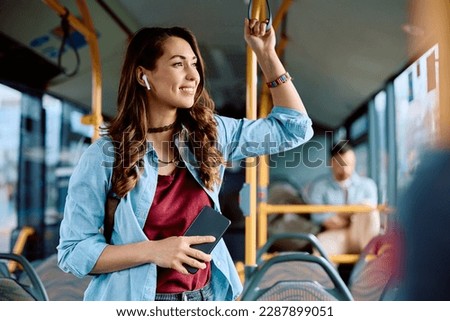 Young smiling woman listening music over earphones while commuting by public transport. 