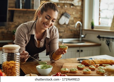 Young smiling woman making avocado bruschetta in the kitchen.  - Powered by Shutterstock