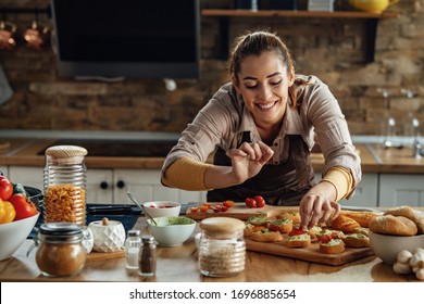 Young smiling woman making bruschetta with healthy ingredients while preparing food in the kitchen.  - Powered by Shutterstock