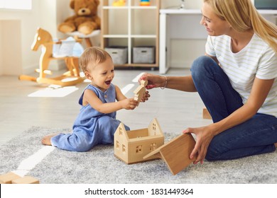 Young smiling woman mother sitting with her small baby boy on floor, giving him wooden toy and playing together at home with room interior at background. Happy childhood and motherhood concept - Powered by Shutterstock