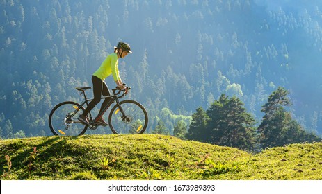 A young smiling woman on a cyclocross bike rides against the background of a green forest on a sunlit meadow