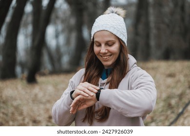 A young smiling woman with orthodontic braces on her teeth checks her fitness tracker while walking on a city park. - Powered by Shutterstock