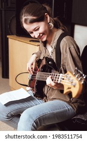 Young Smiling Woman Playing Bass Guitar And Reading Chord Notes At Band Rehearsal. Vertical Size. 