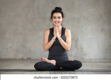 Young smiling woman practicing yoga, doing Padmasana exercise, Lotus pose, working out, wearing sportswear, black pants and top, indoor full length, yoga studio window, looking at the camera - Powered by Shutterstock