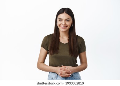 Young Smiling Woman Ready To Offer Her Service, How May I Help You, Holding Hands Clenched Together And Look Friendly At Camera, White Background