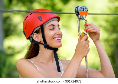 Young and smiling woman in red helmet preparing to ride on a zip line in the forest. Close up view focused on hands and face - Powered by Shutterstock