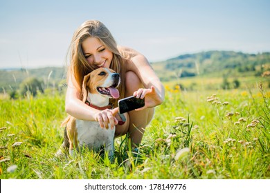 Young smiling woman showing something to her dog on smart-phone, outdoor in nature - Powered by Shutterstock