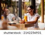 A young smiling woman is sitting alone in a restaurant on a coffee break, having a video call, and having a juice for drink. A woman in a bar using the phone