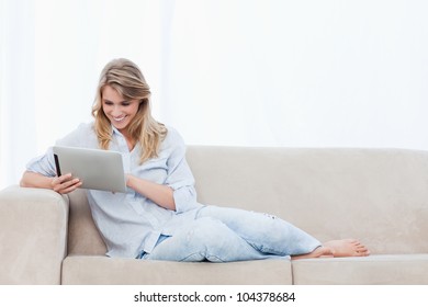 A Young Smiling Woman Sitting On A Couch Is Holding A Tablet