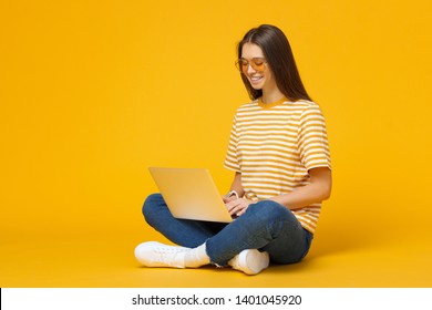 Young Smiling Woman Sitting On Floor With Laptop Isolated On Yellow Background