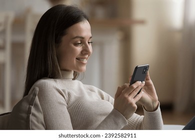 Young smiling woman spend leisure alone at home using modern smartphone browse web page, chatting via social networks enjoy distance communication. E-date on-line services for singles, tech concept - Powered by Shutterstock