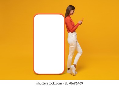 Young smiling woman standing near huge phone mock up for app, isolated on yellow background