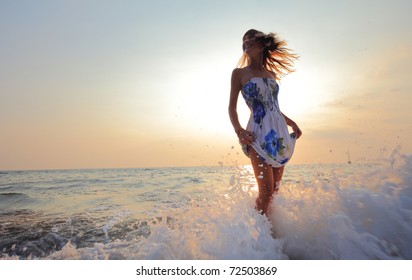 Young smiling woman standing in sea waves and holding her dress - Powered by Shutterstock