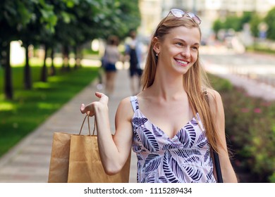 Young Smiling Woman In Sunglasses With Shoping Bag Walk On Street. Blurry Street Background. Shopping Concept