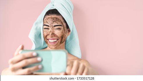 Young Smiling Woman Taking Selfie While Doing Coffee Scrub Facial Mask - Happy Girl Having Skin Care Spa Day At Home - Healthy Alternative Natural Exfoliation Treatment And Technology Concept