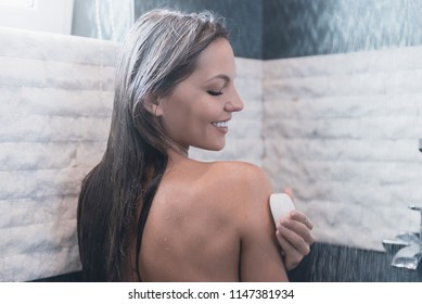 Young Smiling Woman Taking Shower Her Eyes Closed With Pleasure. Pleasant Water Running. Beauty Concept Photo. Cute Brunette Washes With Soap In Bathroom. Personal Hygiene At Morning.