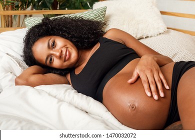 Young smiling woman touching her belly. Pregnant female lying on a bed.