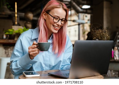 Young smiling woman using laptop while drinking coffee in cafe - Shutterstock ID 1971708110