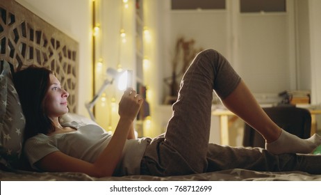 Young smiling woman using smartphone for sharing social media lying in bed at home at night - Powered by Shutterstock