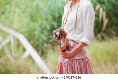 Young smiling woman in vintage style clothes with retro camera against the background of reeds on the lake. Crop photo