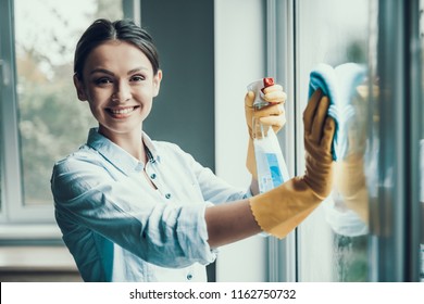 Young Smiling Woman Washing Window with Sponge. Happy Beautiful Girl wearing Protective Gloves Cleaning Window by spraying Cleaning Products and wiping with Sponge. Woman Cleaning House - Powered by Shutterstock