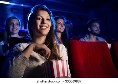 Young Smiling Woman Watching A Film In The Movie Theater And Eating Popcorn, Entertainment And Cinema Concept