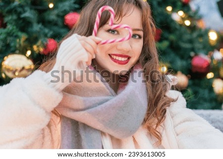 Young smiling woman watching through heart shape made with candy canes on a decorated Christmas tree background. Happy New Year celebration Christmas holidays. Time to share love, and charity concept.
