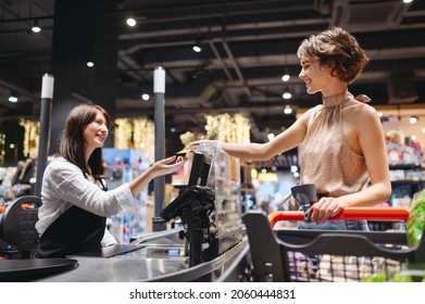 Young Smiling Woman Wear Casual Clothes Mask Shopping At Supermaket Stand At Store Checkout Giving Credit Card To Cashier Pay Inside Hypermarket. People Lifestyle Purchasing Gastronomy Food Concept