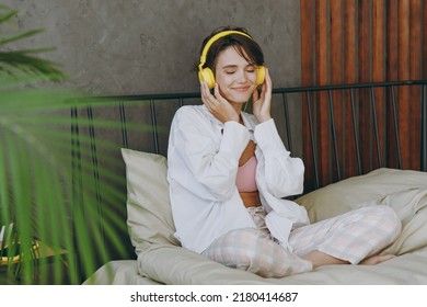 Young Smiling Woman Wear White Shirt Pajama Headphones She Lying In Bed Listen To Music Rest Relax Spend Time In Bedroom Lounge Home In Own Room Hotel Wake Up Dream Be Lost In Reverie Good Mood Day.