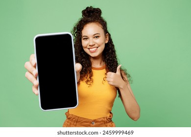 Young smiling woman wear yellow tank shirt top hold in hand use close up mobile cell phone with blank screen workspace area show thumb up isolated on plain pastel green background. Lifestyle concept - Powered by Shutterstock