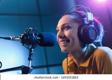 Young smiling woman wearing headphones and talking into a microphone at the radio station, entertainment and communication concept - Powered by Shutterstock