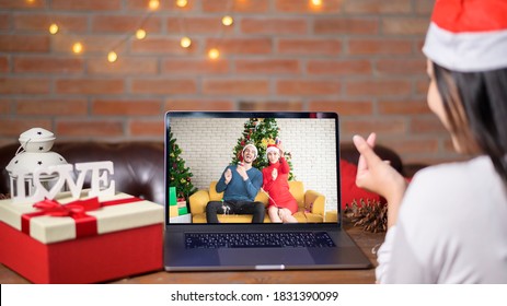A young smiling woman wearing red Santa Claus hat making video call on social network with family and friends on Christmas day.