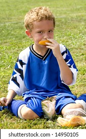 Young Soccer Player Having Halftime Snack Of Orange And Drink Pouch