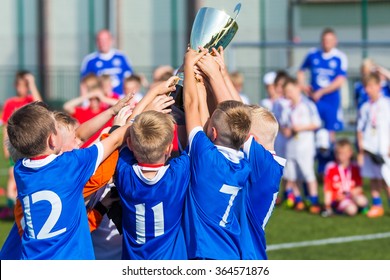 Young Soccer Players Holding Trophy. Boys Celebrating Soccer Football Championship. Winning Team Of Sport Tournament For Kids Children.