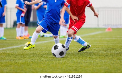 Young soccer players kicking football ball.  Boys play soccer on sports field.