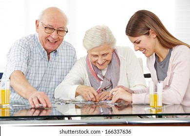 A young social worker solving jigsaw puzzle with senior couple at home - Powered by Shutterstock