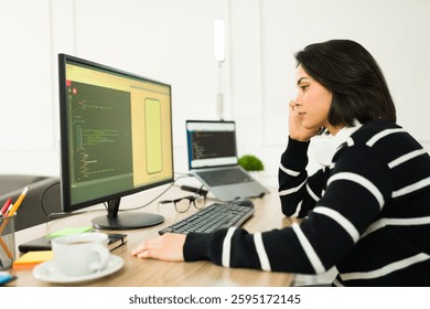 Young software developer working remotely and writing code for a new smartphone app while sitting at her desk