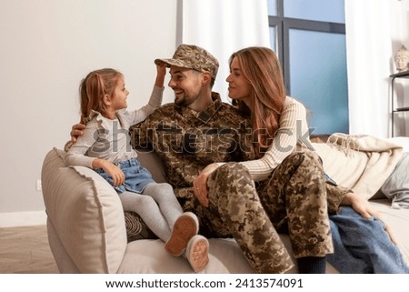 young soldier of the Ukrainian army in a camouflage uniform returned home to his family, a military dad hugs his little daughter and wife at home, a happy military family sits at home on the sofa and