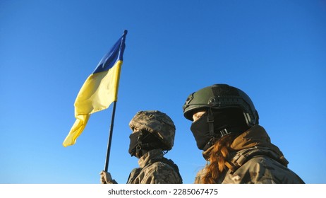 Young soldiers of ukrainian army standing at peak of hill with raised flag of Ukraine. Military couple in camouflage uniform taking each other hands as a symbol of support. Victory at war. Crane shot. - Powered by Shutterstock