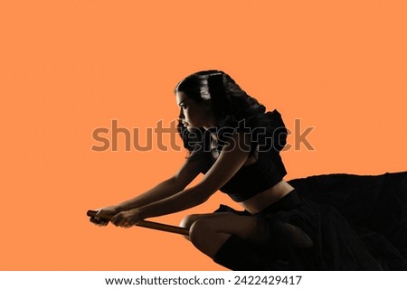 Young sorceress woman flying on broom to Halloween carnival event, Enchanting orange aura: Backgrounded brunette woman embodies a mystical sorceress allure.