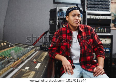 Young sound operator sitting by soundboard in her record studio