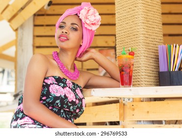 Young South African Zulu Woman Is Sitting Near Bar And Drinking Mojito, Summer Time With Fashion Makeup Is Wearing Pink Turban Fashion Dress And Bead