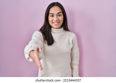 Young South Asian Woman Standing Over Pink Background Smiling Friendly Offering Handshake As Greeting And Welcoming. Successful Business. 