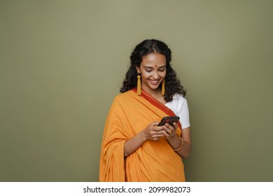 Young South Asian Woman Wearing Sari Smiling While Using Mobile Phone Isolated Over Green Wall