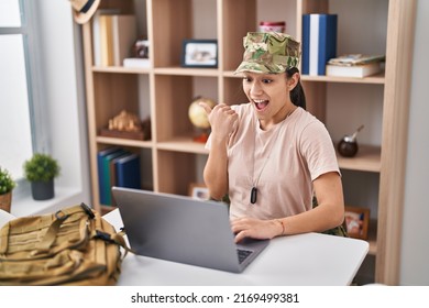 Young South Asian Woman Wearing Camouflage Army Uniform Doing Video Call Pointing Thumb Up To The Side Smiling Happy With Open Mouth 