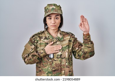 Young South Asian Woman Wearing Camouflage Army Uniform Swearing With Hand On Chest And Open Palm, Making A Loyalty Promise Oath 