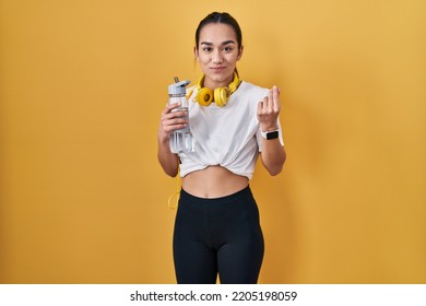 Young South Asian Woman Wearing Sportswear Drinking Water Doing Money Gesture With Hands, Asking For Salary Payment, Millionaire Business 