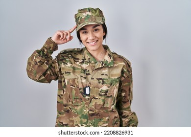 Young South Asian Woman Wearing Camouflage Army Uniform Smiling Pointing To Head With One Finger, Great Idea Or Thought, Good Memory 